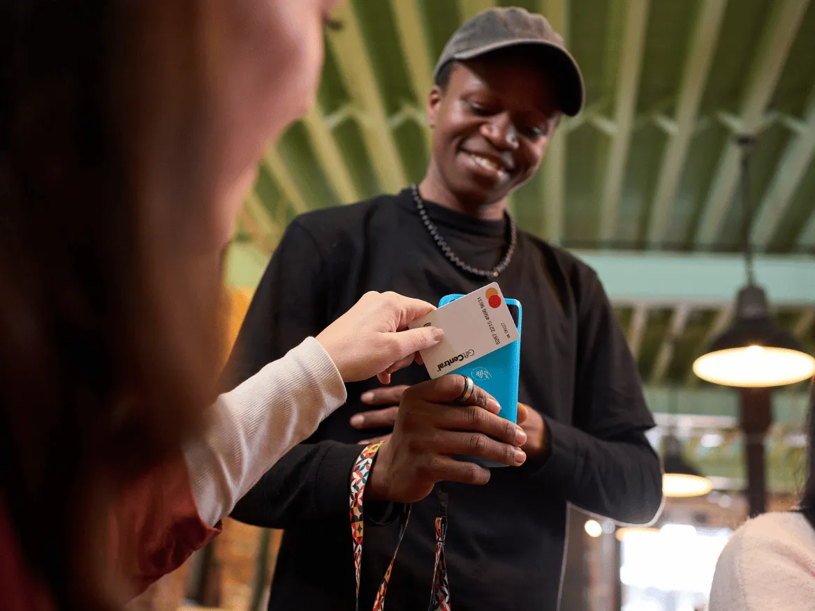 Customer tapping a bank card on a blue Yoco card machine held by a merchant.