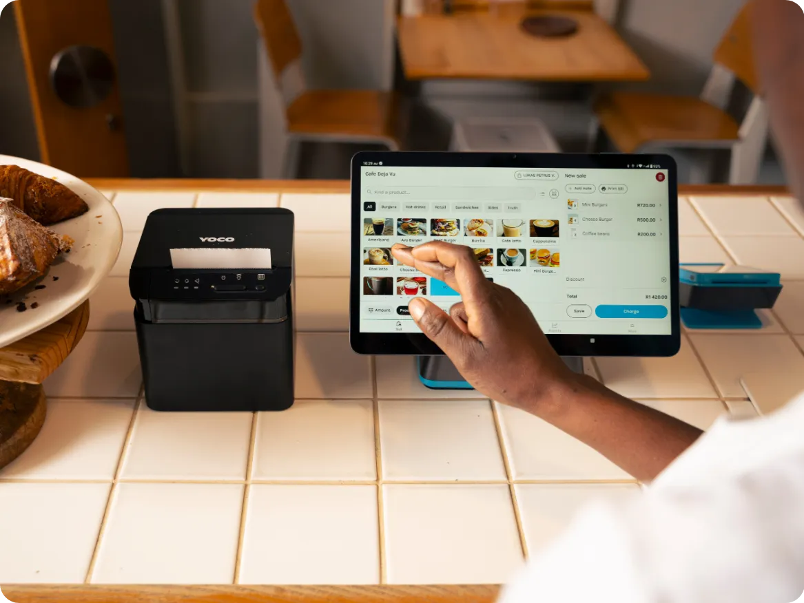 Hand selecting products on a point of sale screen beside a receipt printer