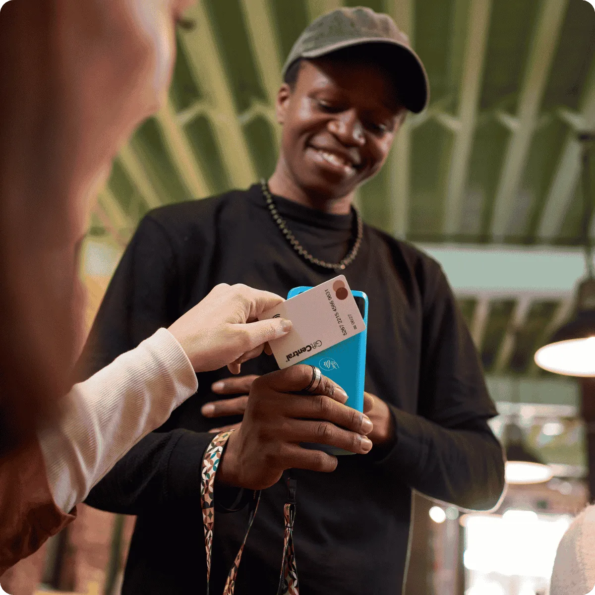 Customer tapping a bank card on a blue Yoco card machine held by a merchant.