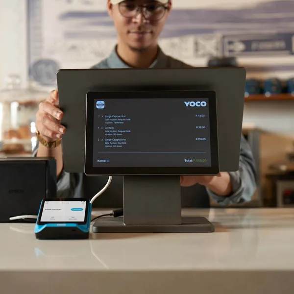 Waiter using Table by Yoco POS system in a restaurant to manage orders and payments at the counter.