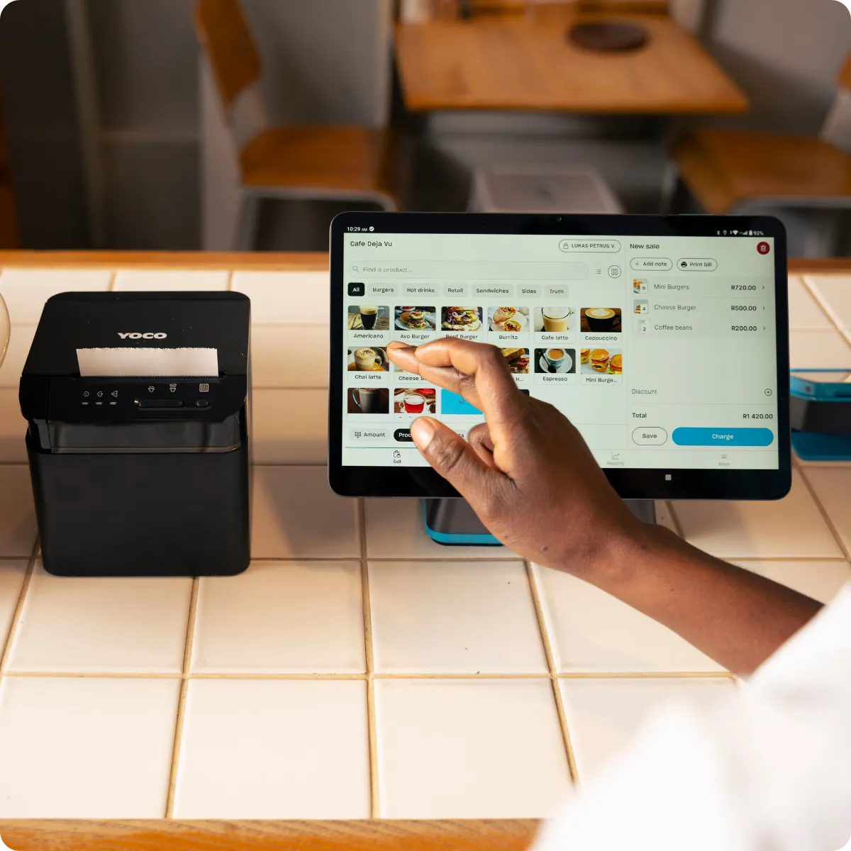 Hand selecting products on a point of sale screen beside a receipt printer