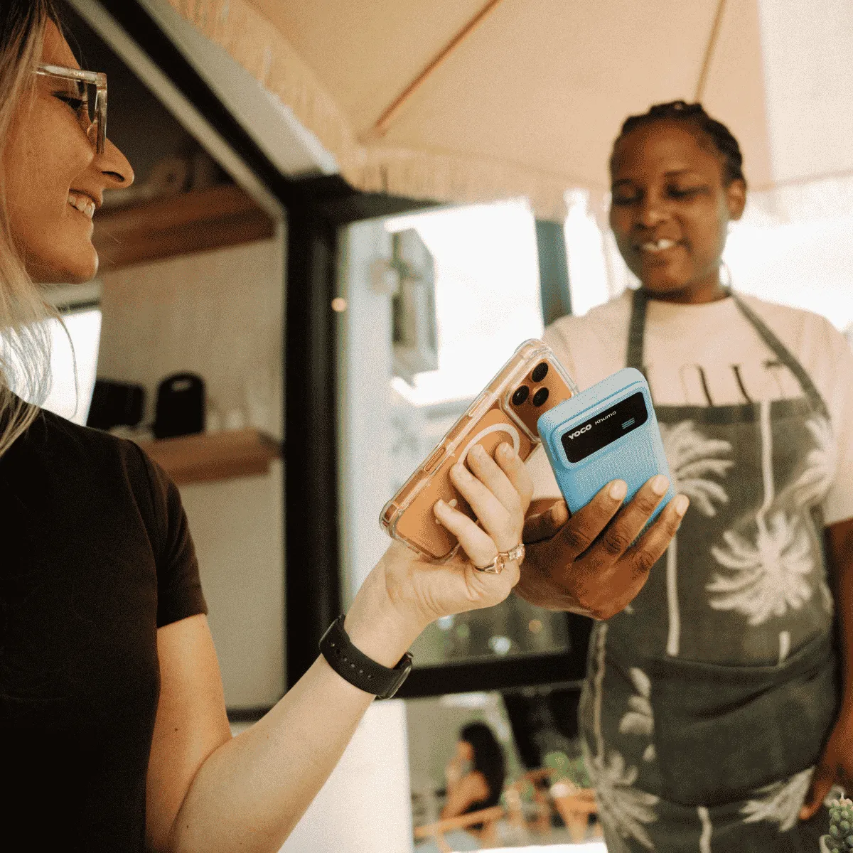 Customer tapping a smartphone on a Yoco card machine at an outdoor market 1:1
