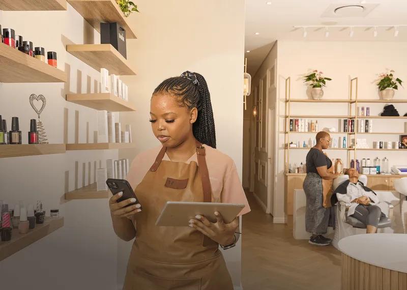 Beauty salon employee using a tablet and phone while a client receives a hair treatment.