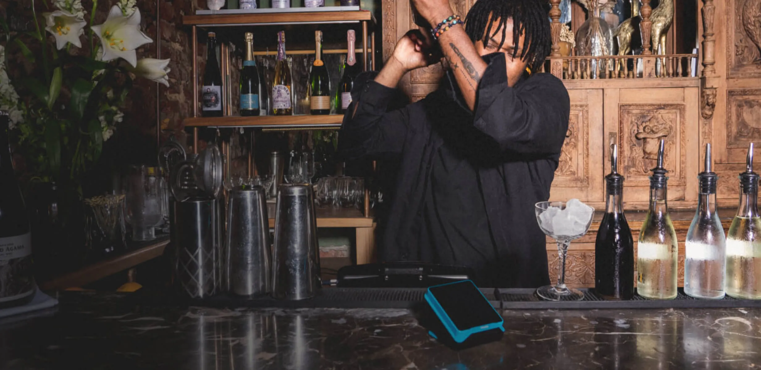 A bartender prepares a drink behind a bar, with a Yoco card machine on the counter.