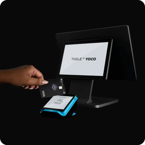 Table by Yoco POS system with card payment terminal, showing a customer tapping a Visa card for contactless payment.
