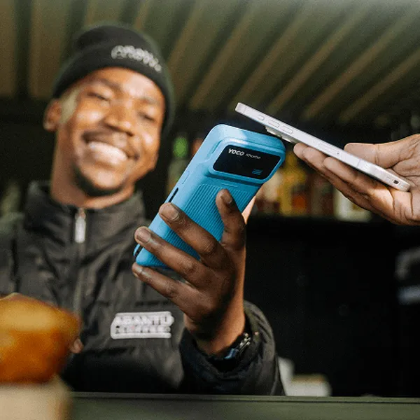 Smiling merchant accepting a customer’s contactless smartphone payment on a handheld card machine.