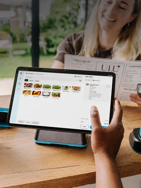 Tablet-based POS system in use, with a server managing a customer’s order on-screen while the customer reviews a menu, illustrating full-service digital checkout.